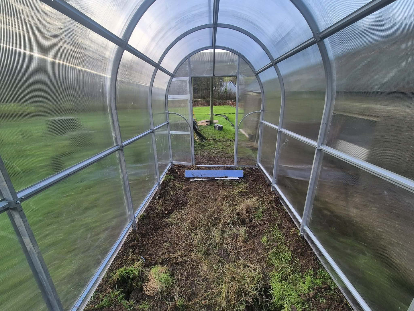 Sigma 200 (Gen III) Greenhouse interior with soil floor and glass walls, outside view of grassy field.