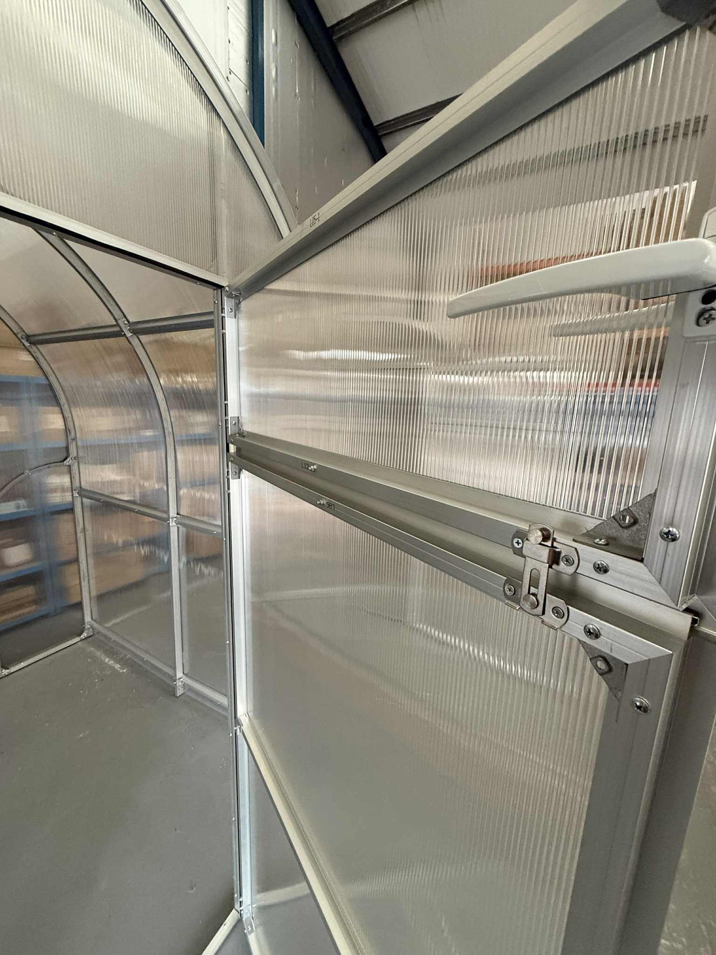 Partial view of a Sigma 200 (Gen III) greenhouse with transparent panels and metal frame.