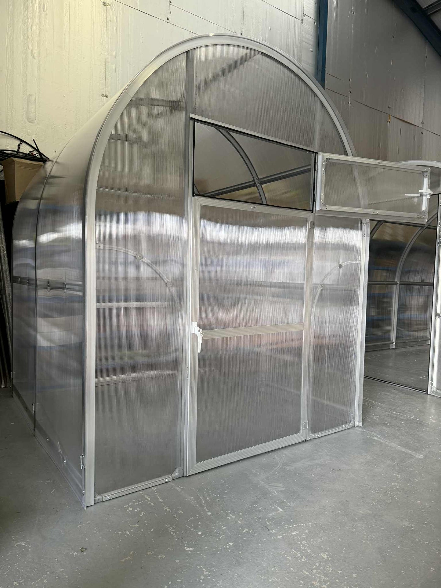 Clear polycarbonate Sigma 200 (Gen III) greenhouse structure with metal frame in a warehouse setting
