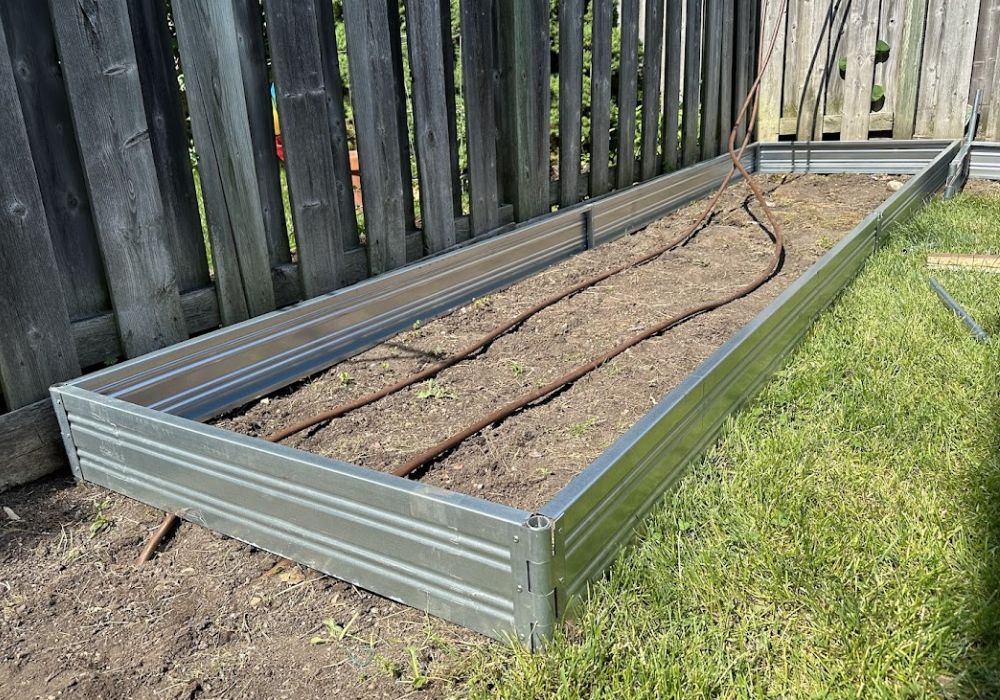 Metal raised Planta garden bed - 1 tier against a wooden fence with soil inside