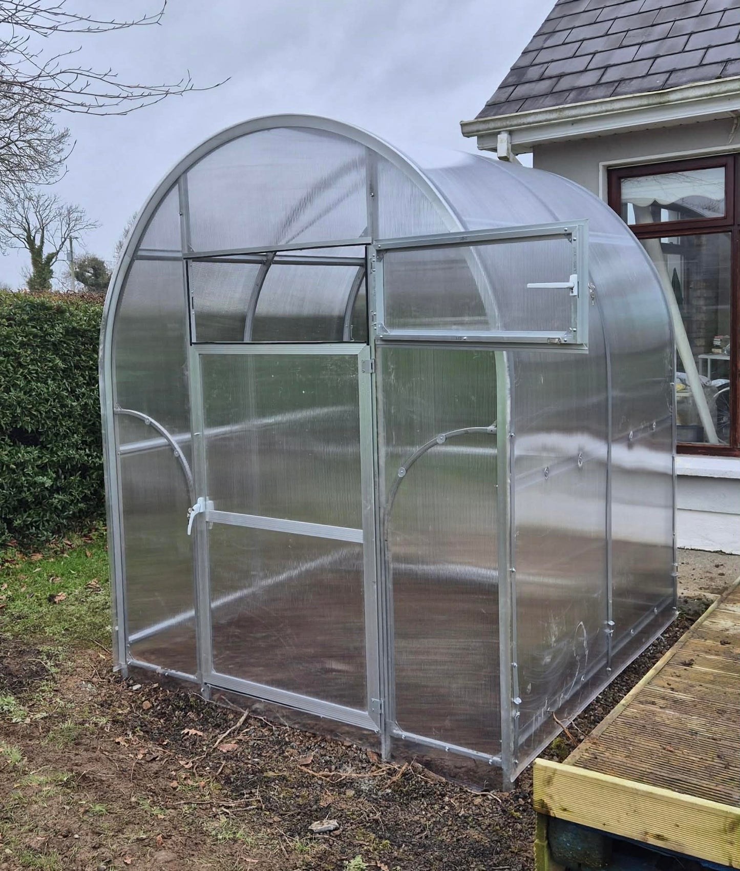 Small Sigma 2x4 (Gen III) greenhouse on a garden with a house in the background